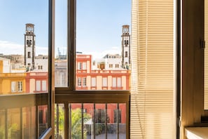 A window with a view of buildings, including a clock tower, through a window with blinds.