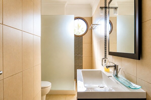 A modern bathroom with a large sink, a toilet, and a shower with a circular window.