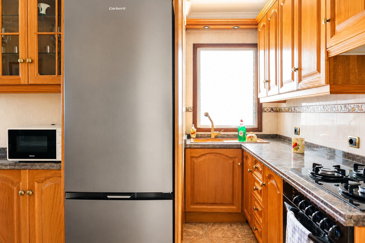 A kitchen with wooden cabinets, a stainless steel refrigerator, a microwave, a sink with a faucet, and a stove.