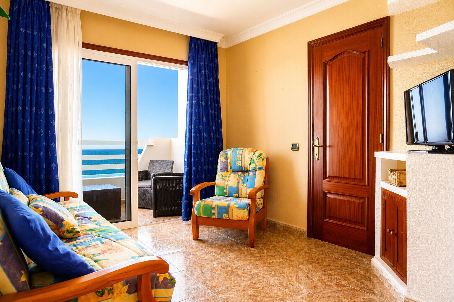 A room with a sofa, a chair, a wooden door, and a television.