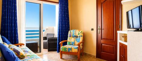 A room with a sofa, a chair, a wooden door, and a television.