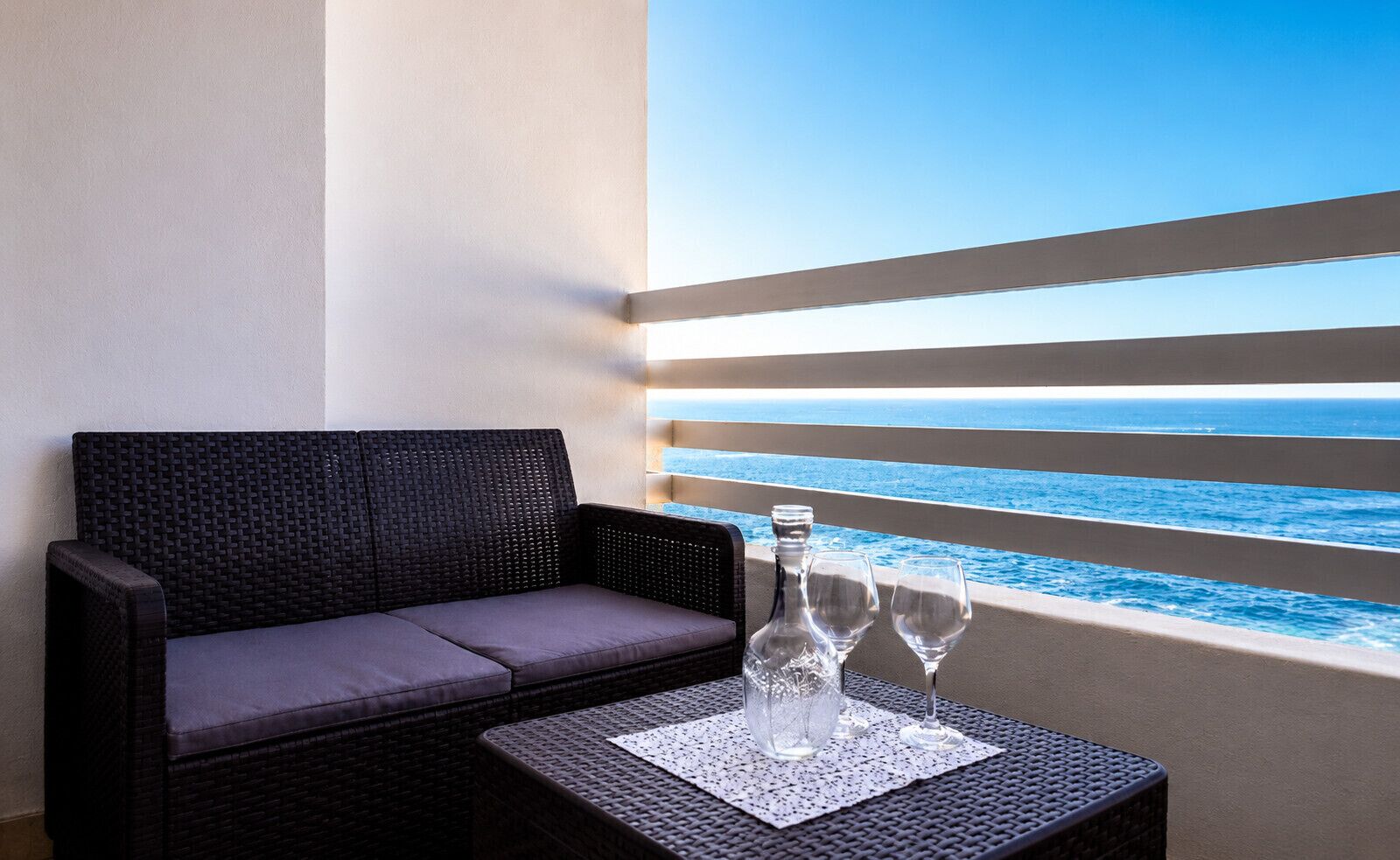 Een balkon met een rieten bank, een tafel met een fles en glazen, en uitzicht op de oceaan.