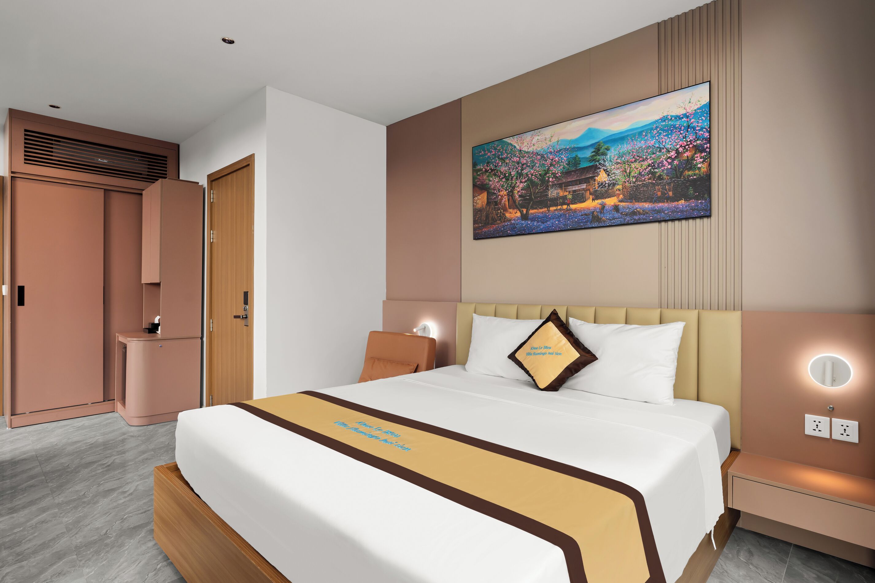 A hotel room with a large bed, a painting on the wall, a bedside table, and a wardrobe.