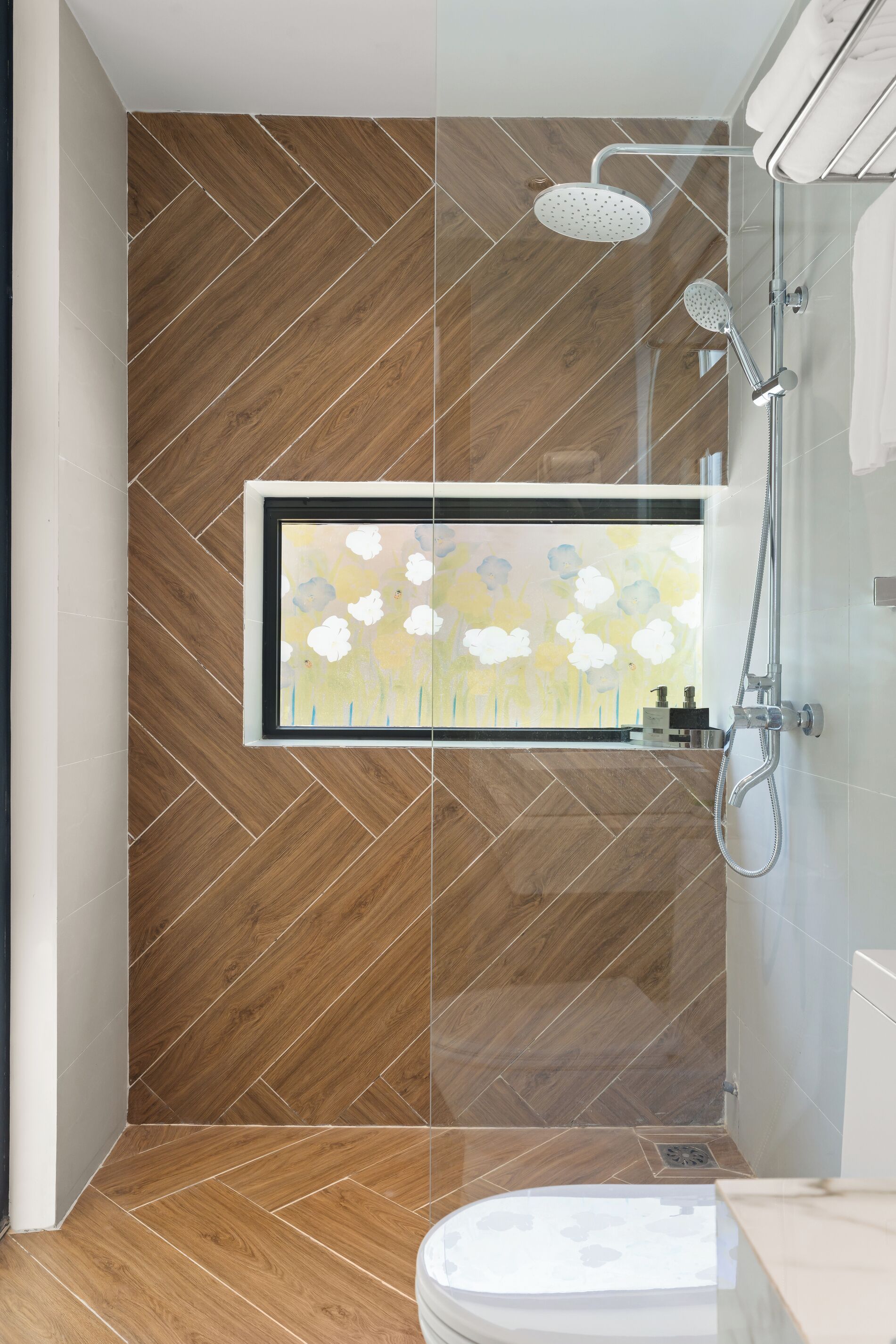 Une salle de bain moderne avec un parquet en bois disposé en chevrons, une œuvre d’art encadrée et une douche équipée d’un pommeau de douche amovible.
