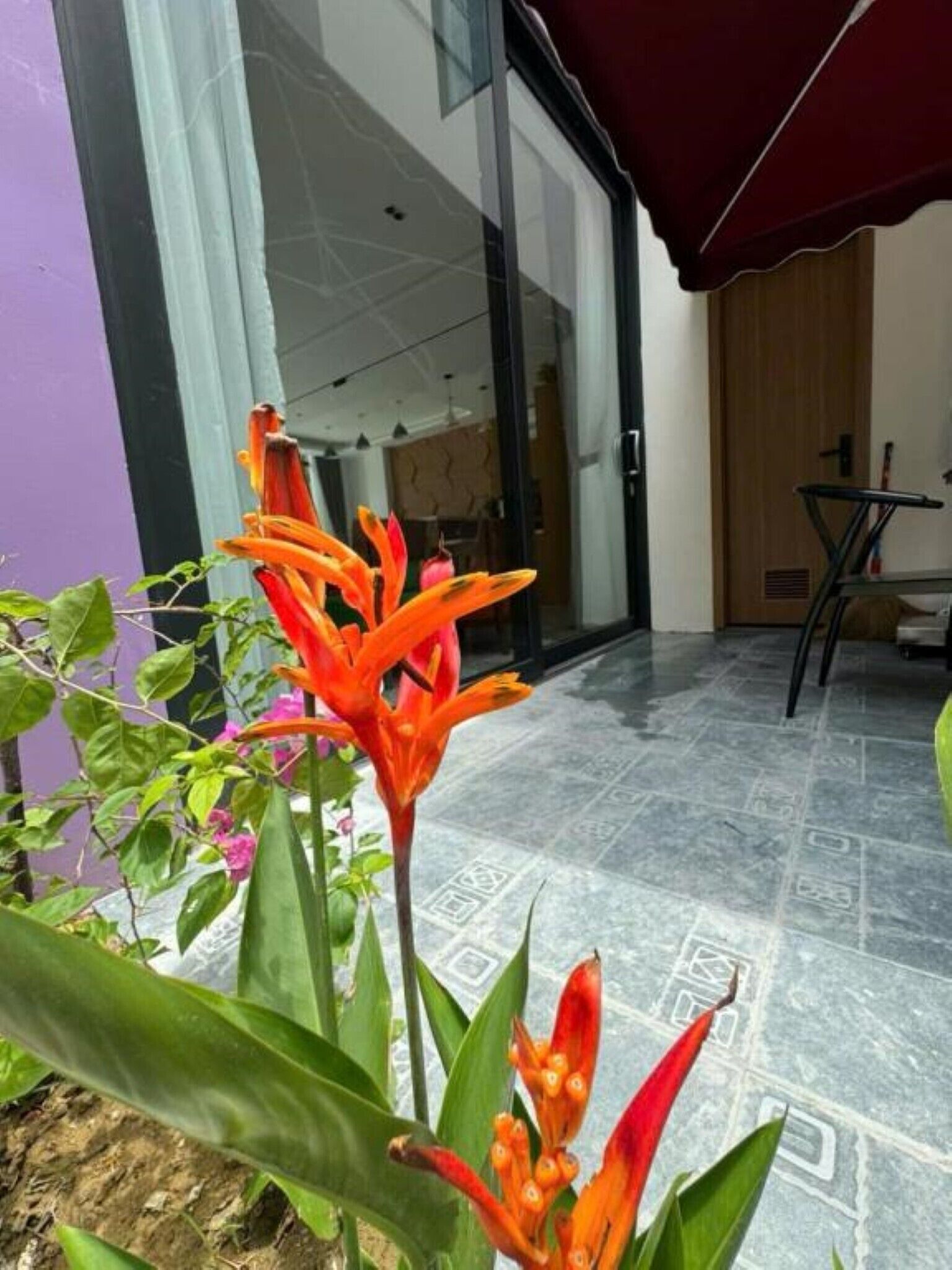 A modern building with a glass entrance, a red awning, and a tiled patio area.