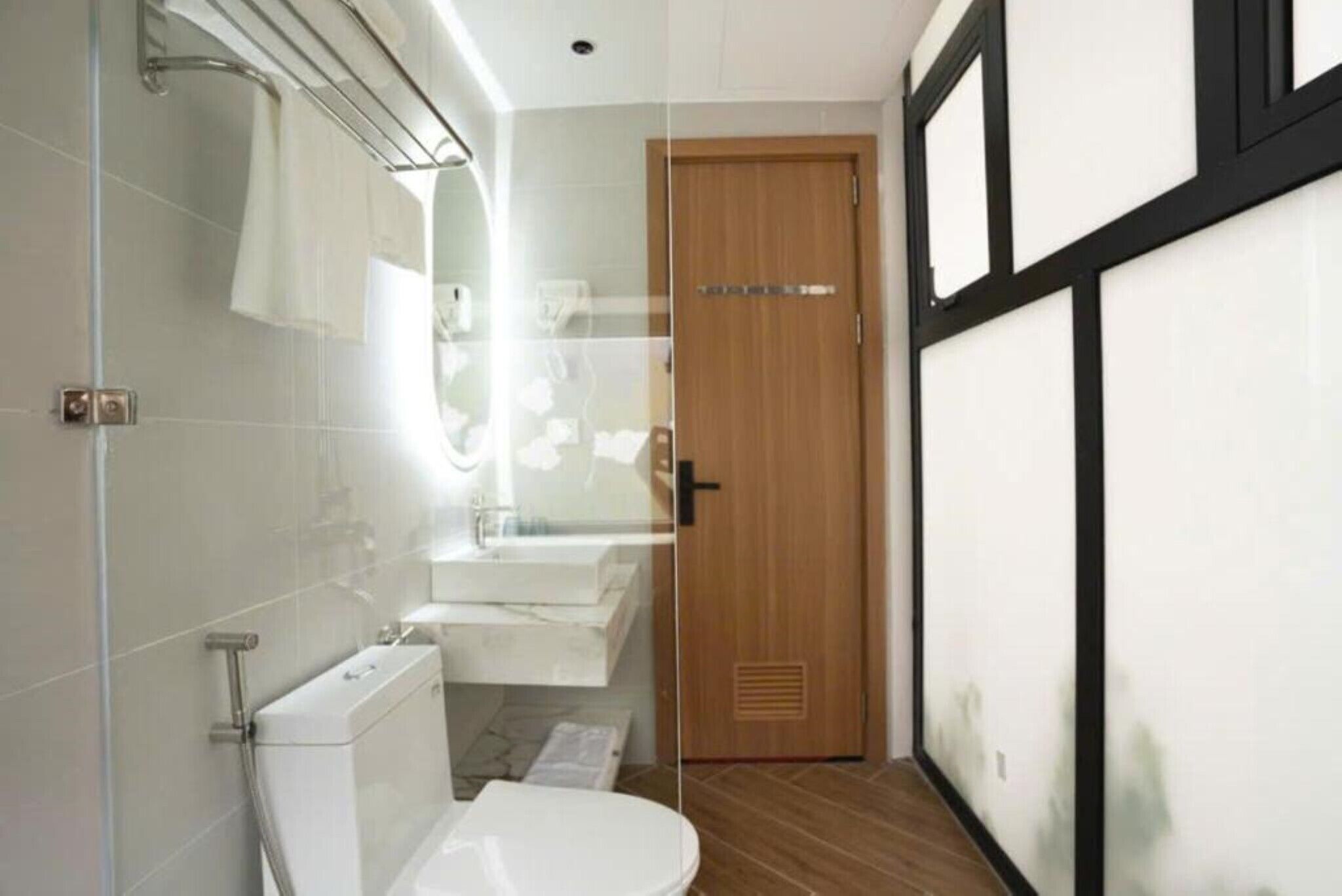 A modern bathroom with a glass shower enclosure, a white toilet, and a wooden door.