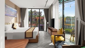 A modern hotel room with a large bed, a desk, a chair, and a balcony with a view of the city.