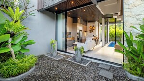 A modern house with a glass door leading to a living area, a pool, and a stone wall.
