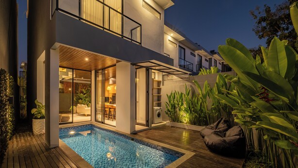 A modern house with a swimming pool, wooden deck, and a dining area.