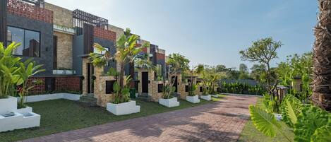 Un moderno edificio residencial con un sendero pavimentado, macetas blancas y plantas tropicales.