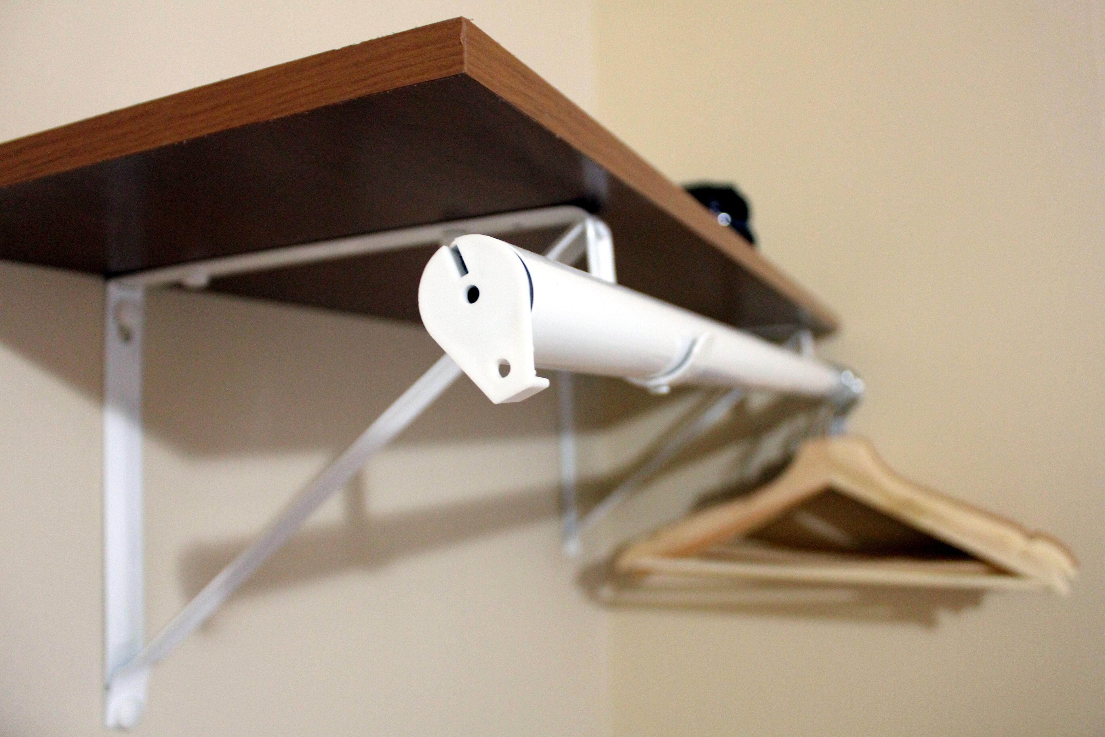 A white ceiling-mounted device, possibly a light or sensor, attached to a wooden shelf with a metal frame.