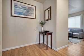 A hallway with a wooden floor, a framed painting, a mirror, and a vase with greenery. - Brighton Guesthouse Private Rooms  (Seattle)