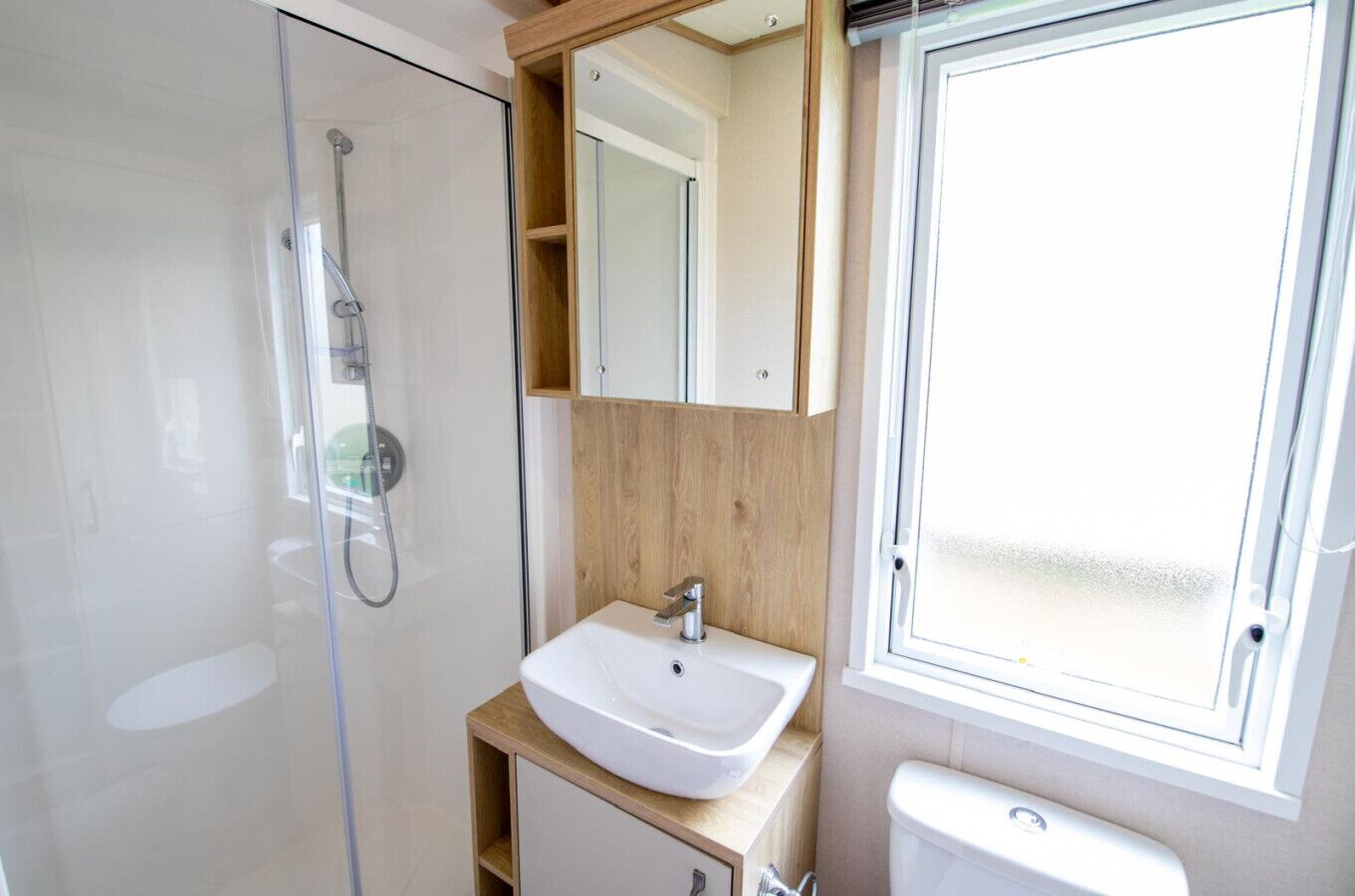 A modern bathroom with a glass shower enclosure, a wooden vanity with a sink, and a toilet.