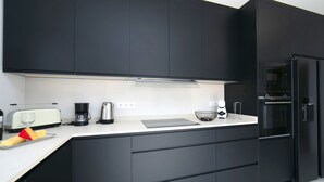 A modern kitchen with dark cabinetry, a white countertop, a toaster, a coffee maker, and a refrigerator. - Vacation home Isa by Interhome (Benissa)