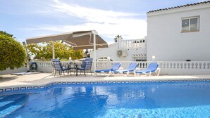 A clear swimming pool with lounge chairs and a table, surrounded by a white building with a balcony. - Vacation home Isa by Interhome (Benissa)