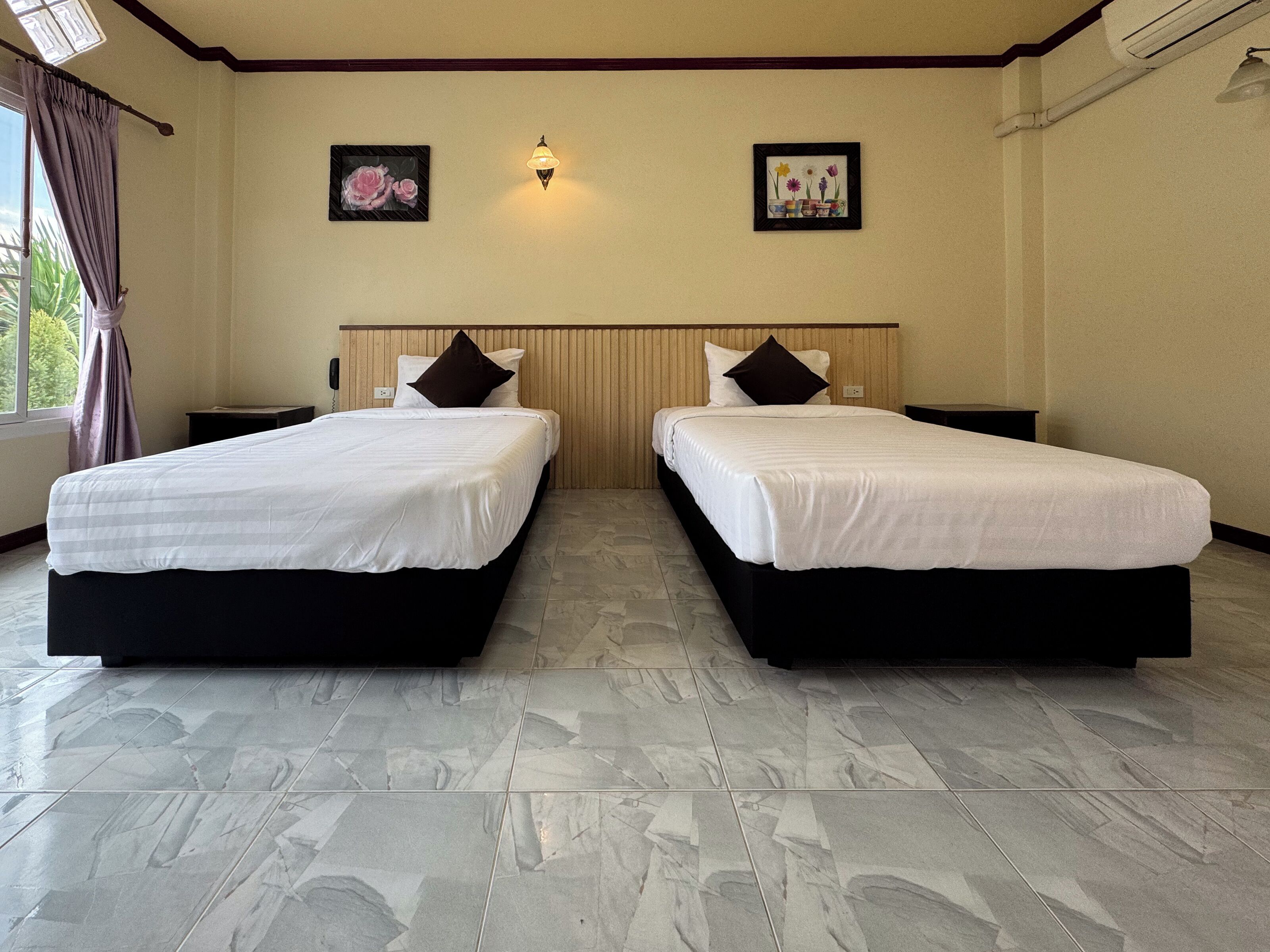 Quarto de hotel com duas camas, cabeceira de madeira, luz acoplada à parede e janela com cortinas.