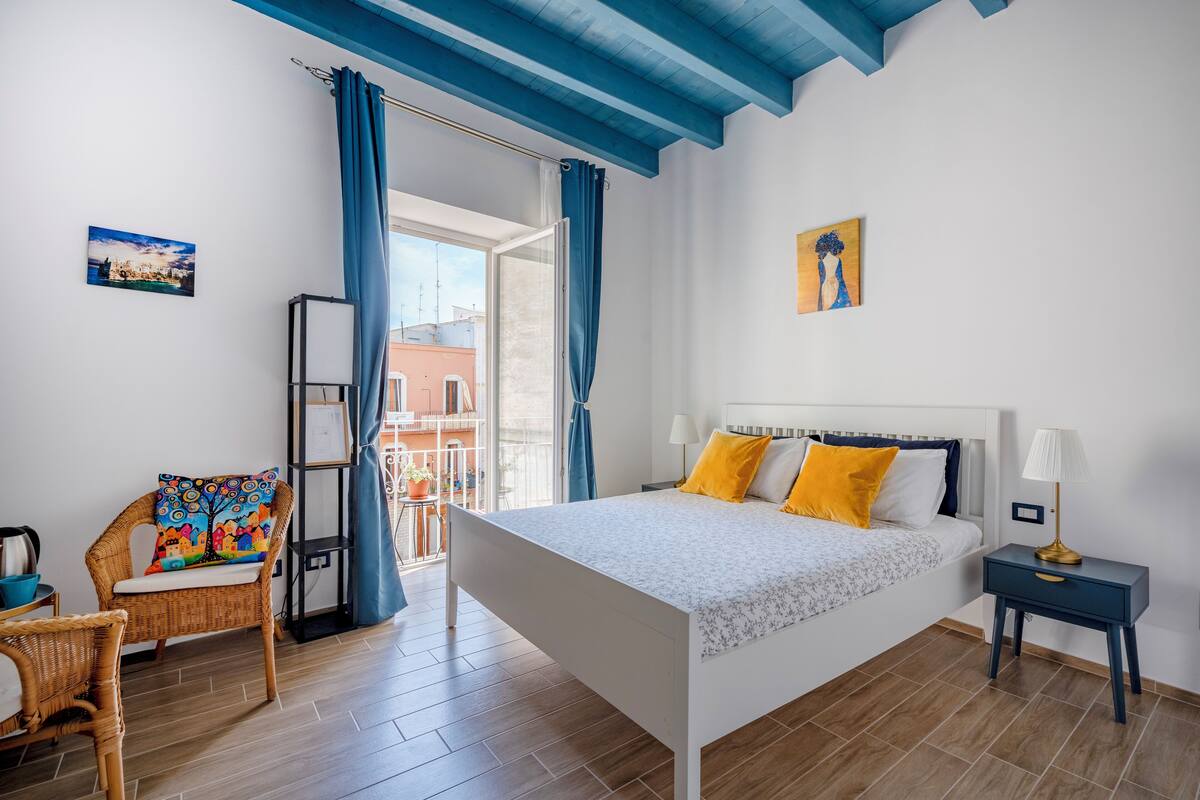 Une chambre à coucher avec un lit, une chaise, une table de chevet et une vue sur l’extérieur.