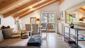 A cozy room with a sloped ceiling, a sofa, chairs, a table, a mirror, and a view through a glass door. - Apartment 'Place In The Bavarian Mountains' with Mountain View, Private Garden and Wi-Fi (Schneizlreuth)