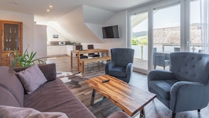 Een moderne woonkamer met een bank, fauteuils, een houten salontafel en een aan de muur bevestigde televisie.