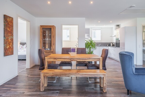 A modern dining area with a wooden table and chairs, a glass cabinet, and a view into the kitchen.