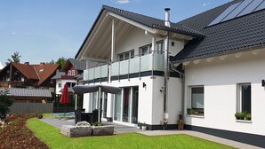 Een modern herenhuis met balkon, grote ramen en een verzorgd gazon.