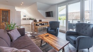 Un salon moderne avec un canapé, des fauteuils, une table basse en bois et un téléviseur fixé au mur.