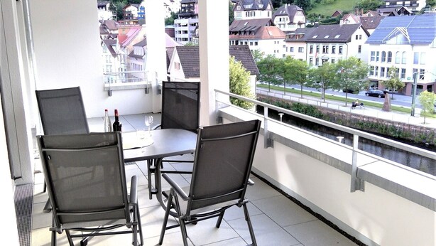 A balcony with a table and chairs, overlooking a residential area with houses and a river.
