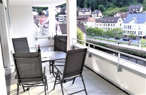 Un balcón con mesa y sillas, con vista a una zona residencial con casas y un río.