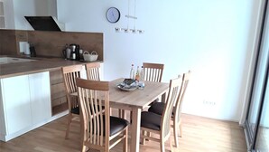 A modern kitchen with a dining area, wooden chairs, a wooden table, and a clock on the wall.