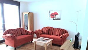 A living room with two red sofas, a wooden coffee table, a TV stand, and a painting on the wall.