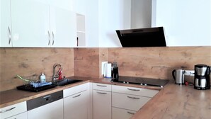 A modern kitchen with white cabinets, a wooden countertop, a dishwasher, a coffee maker, and a kettle.