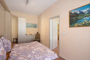 A bedroom with a bed, a desk, a chair, and a painting on the wall.