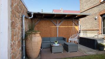 A patio with a stone wall, a wooden fence, a grey sofa, a white chair, and a large planter.