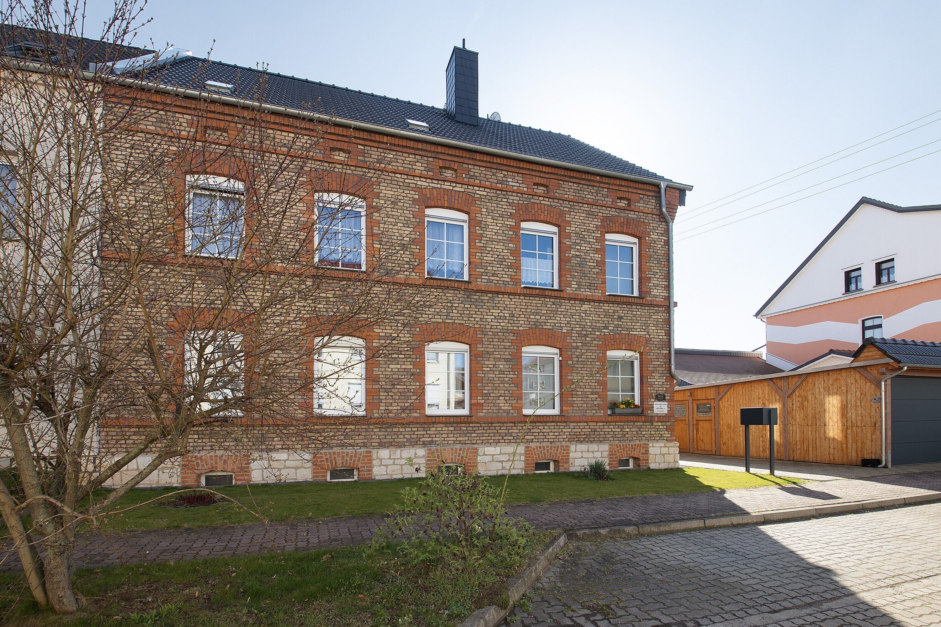 Ein Backsteinhaus mit mehreren Fenstern und einer gepflasterten Auffahrt.
