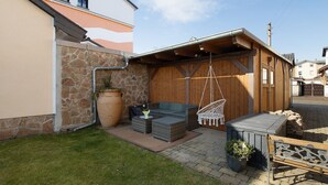 Patio esterno con pavimento in legno, parete in pietra e una sedia a dondolo.