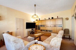 A living room with a sofa, a coffee table, a television, and a kitchen area with cabinets and a sink.