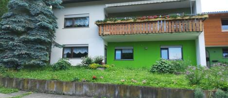 Un edificio de dos pisos con un balcón, una puerta verde y una antena parabólica.