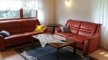 Un salon comprenant un canapé, un fauteuil, une table basse et une vue par la fenêtre.