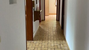 Un pasillo con suelo de baldosas, puertas de madera y un interruptor de luz en la pared.