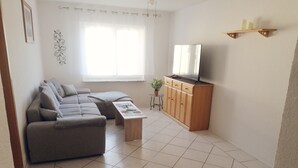 A living room with a sofa, a coffee table, a TV on a wooden cabinet, and a window with curtains. - Holiday Apartment 'Auf Dem Land' with Shared Terrace, Shared Garden and Wi-Fi (Badenhard)