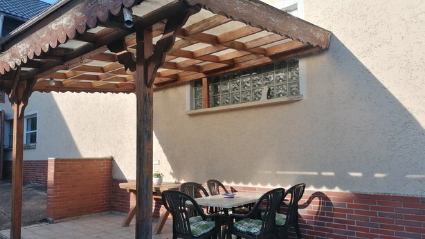 A covered patio with a table and chairs, a brick wall, and a window. - Holiday Apartment 'Auf Dem Land' with Shared Terrace, Shared Garden and Wi-Fi (Badenhard)