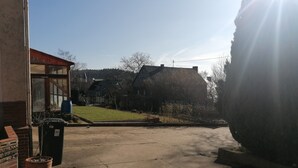 A paved driveway leading to a building with a glass door, a large potted plant, and a grassy area with trees. - Holiday Apartment 'Auf Dem Land' with Shared Terrace, Shared Garden and Wi-Fi (Badenhard)