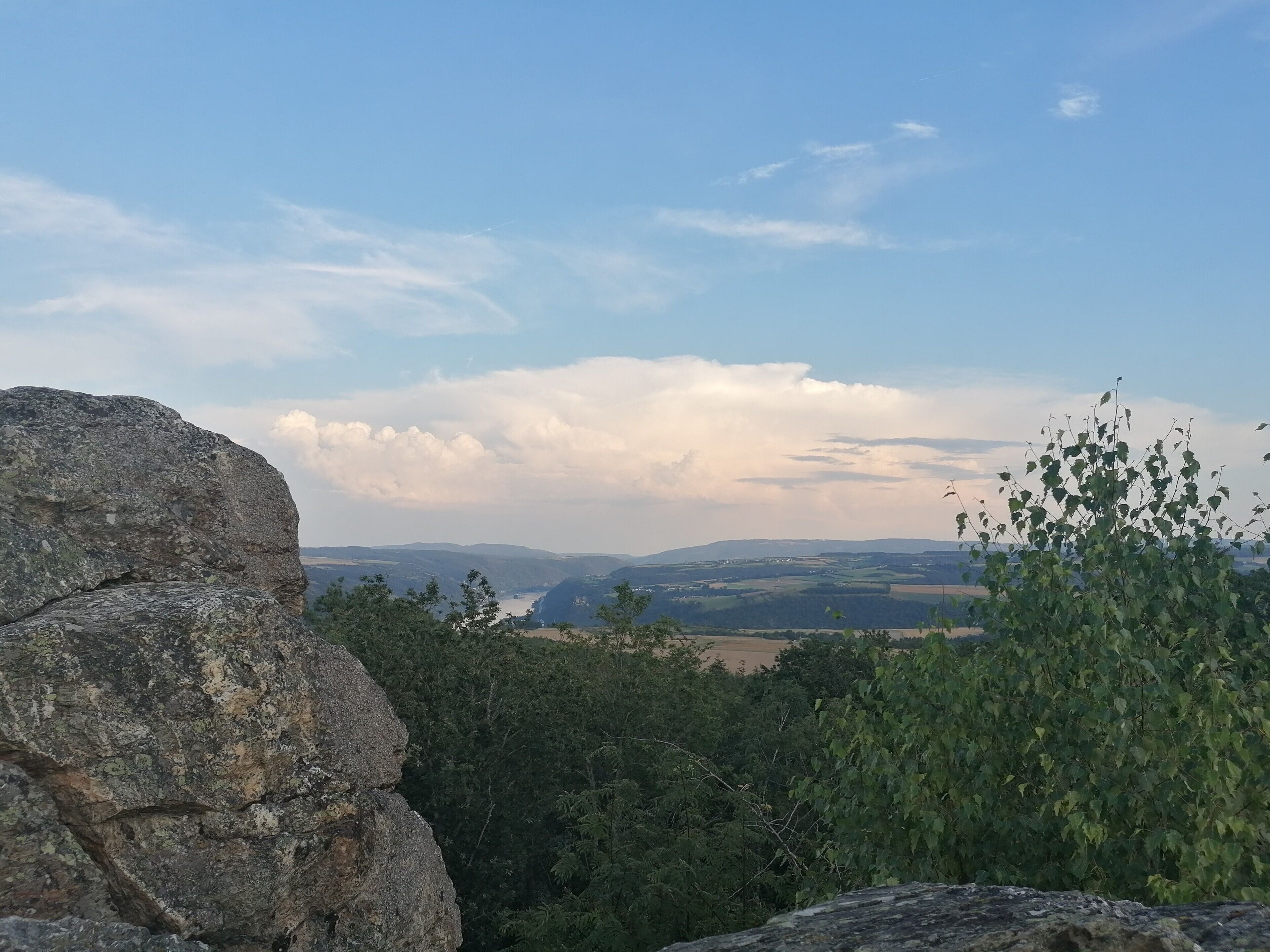 Eine natürliche Landschaft mit einer Felsformation im Vordergrund und Blick auf ferne Hügel unter teils bewölktem Himmel.