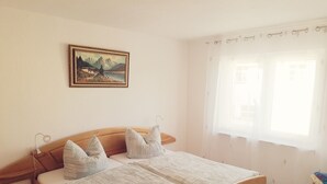 A bedroom with a wooden bed, a painting on the wall, and a window with curtains. - Holiday Apartment 'Auf Dem Land' with Shared Terrace, Shared Garden and Wi-Fi (Badenhard)