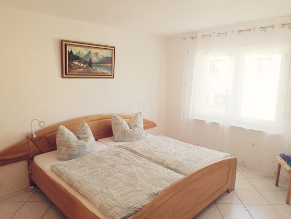 A bedroom with a wooden bed, a painting on the wall, and a window with curtains.