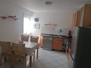 A kitchen with a dining table, chairs, a refrigerator, a sink, and a clock on the wall.