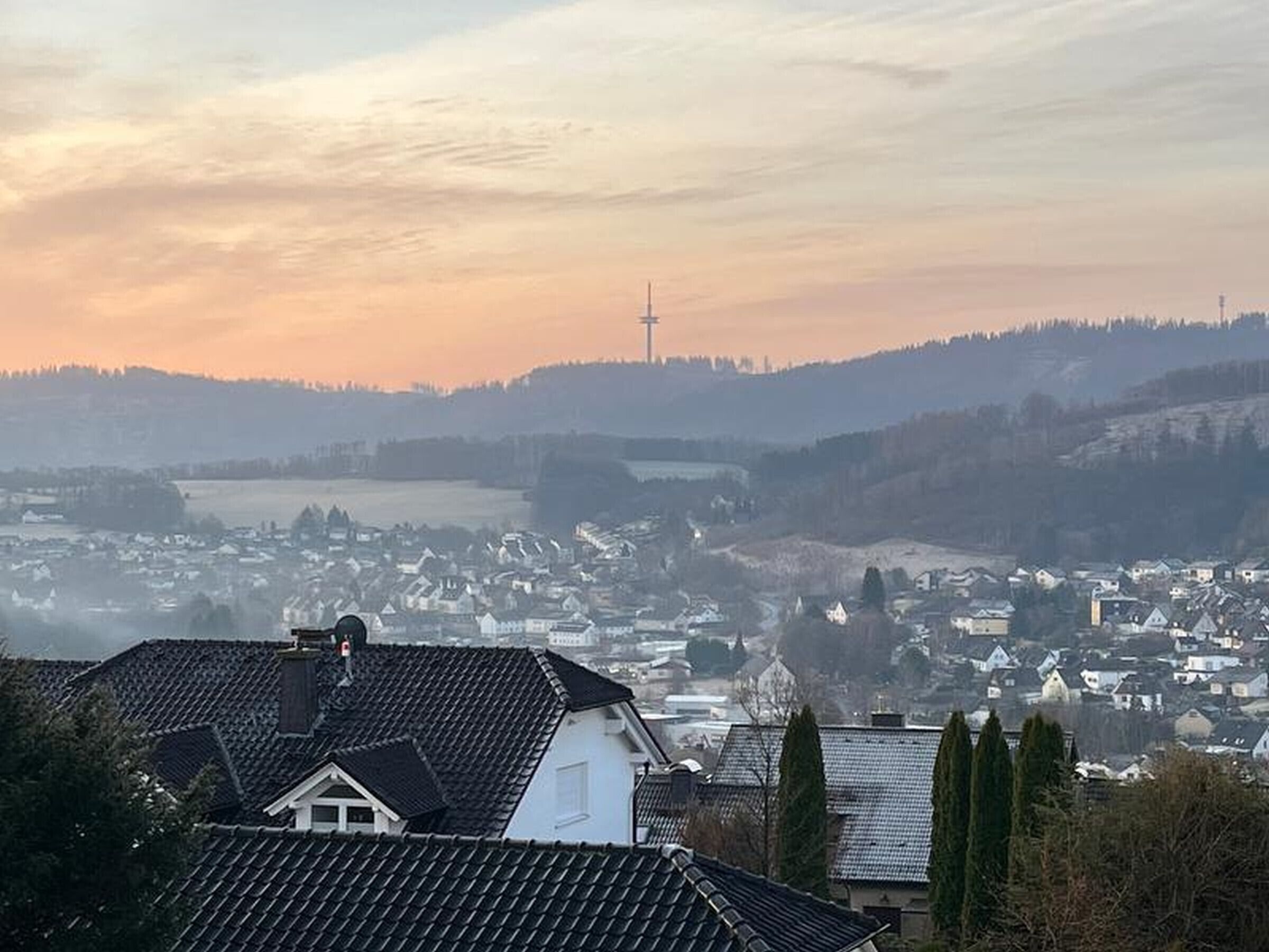 A town with houses, a prominent tower, and a hilly landscape.