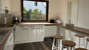 A modern kitchen with white cabinets, a large window, and a bar area with stools. - Apartment "Lavender", 110 sqm with Balcony (Herscheid)