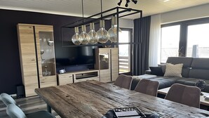 A modern living room with a wooden dining table, a sofa, and a TV. - Apartment "Lavender", 110 sqm with Balcony (Herscheid)