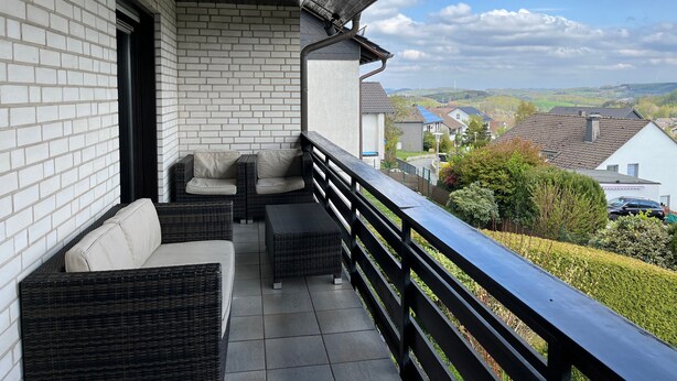 A balcony with wicker furniture, a view of houses, and a clear sky. - Haus Blumenglück "Lavender and Dandelion" – Two Apartments for up to 11 Guests (Herscheid)